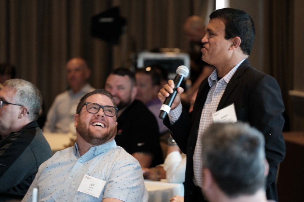 A group of people at a corporate retreat, with one individual speaking into a microphone while others listen and engage, showcasing a lively discussion. Huntington Beach hyatt orange county business corporate event photographer nicole caldwell