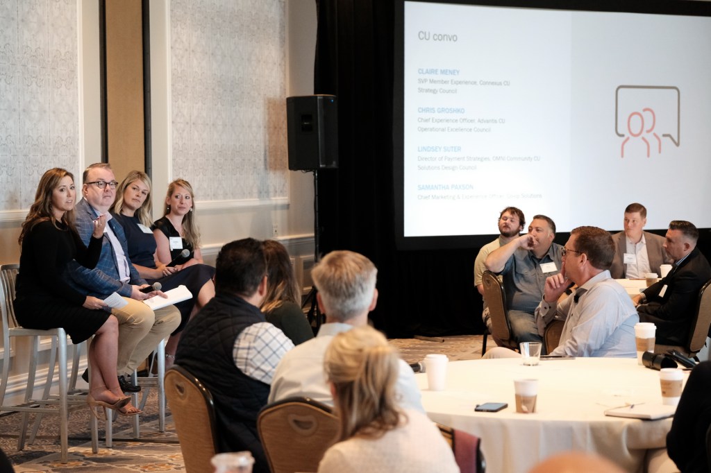 A panel discussion at a corporate retreat with four speakers on stage, discussing various topics, while attendees listen intently at round tables. Huntington Beach hyatt orange county business corporate event photographer nicole caldwell