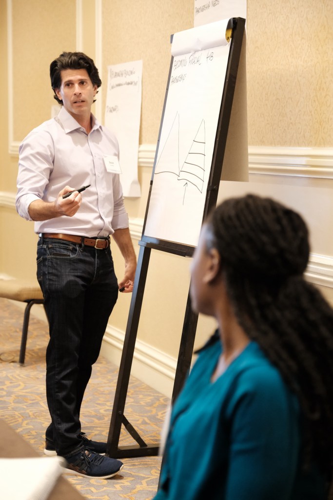 A facilitator presents to a group during a corporate retreat, standing beside a flip chart with a graph. The audience member, partially visible, listens attentively.Huntington Beach hyatt orange county business corporate event photographer nicole caldwell