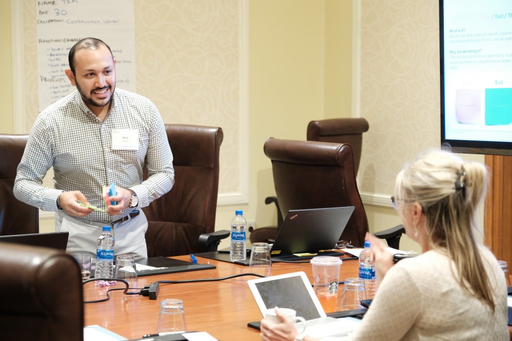 A man presenting to a group during a corporate meeting at a conference table, with laptops and water bottles visible. Huntington Beach hyatt orange county business corporate event photographer nicole caldwell