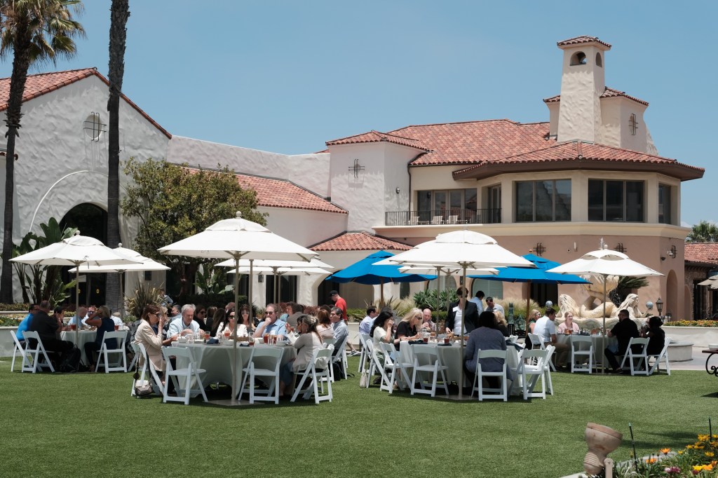 Outdoor corporate retreat event at Hyatt in Huntington Beach, with participants seated at round tables under umbrellas, enjoying lunch on a sunny day. Huntington Beach hyatt orange county business corporate event photographer nicole caldwell