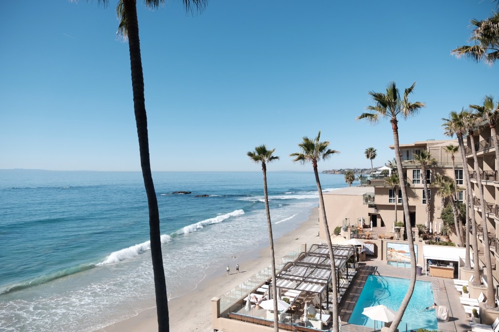 Aerial view of Surf and Sand Resort at Laguna Beach, California, featuring palm trees, a beach, and a swimming pool with lounge chairs. business conference surf and sand hotel laguna beach photographer nicole caldwell