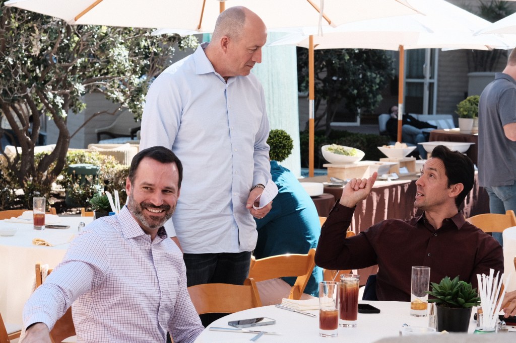 Group of three men engaged in conversation at an outdoor social event, with tables and drinks in the background. business conference surf and sand hotel laguna beach photographer nicole caldwell