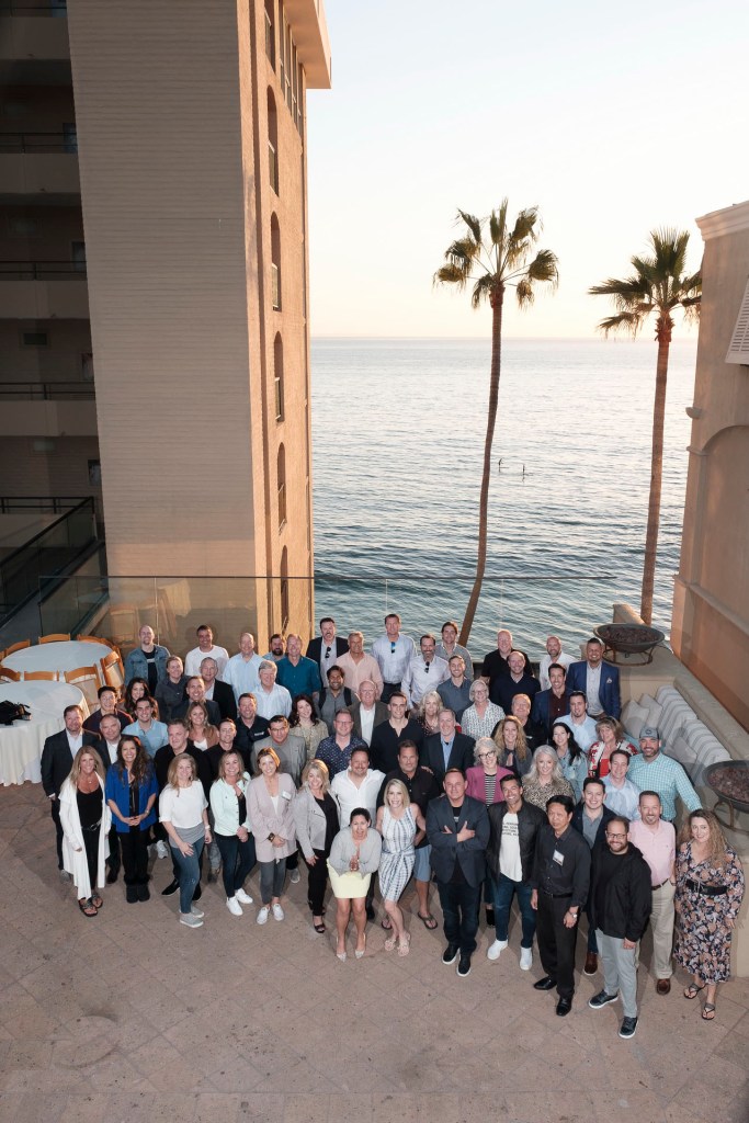 Group photo of attendees at a welcome reception in Laguna Beach, California, with a sunset view and palm trees in the background. business conference surf and sand hotel laguna beach photographer nicole caldwell