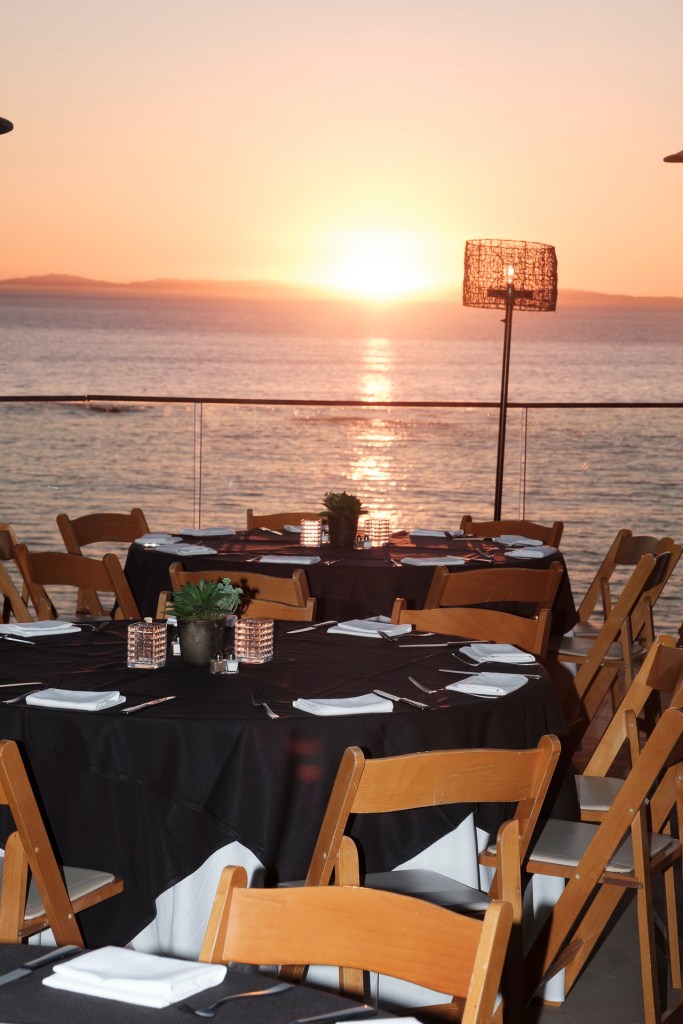 Dining setup with round tables, black tablecloths, and white napkins overlooking a sunset over the ocean. business conference surf and sand hotel laguna beach photographer nicole caldwell