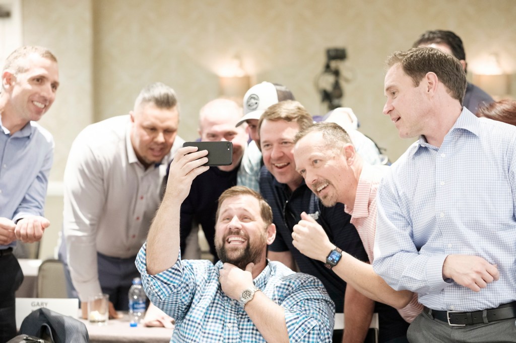 A group of men joyfully taking a selfie together at an event, smiling and interacting in a conference setting. business conference surf and sand hotel laguna beach photographer nicole caldwell