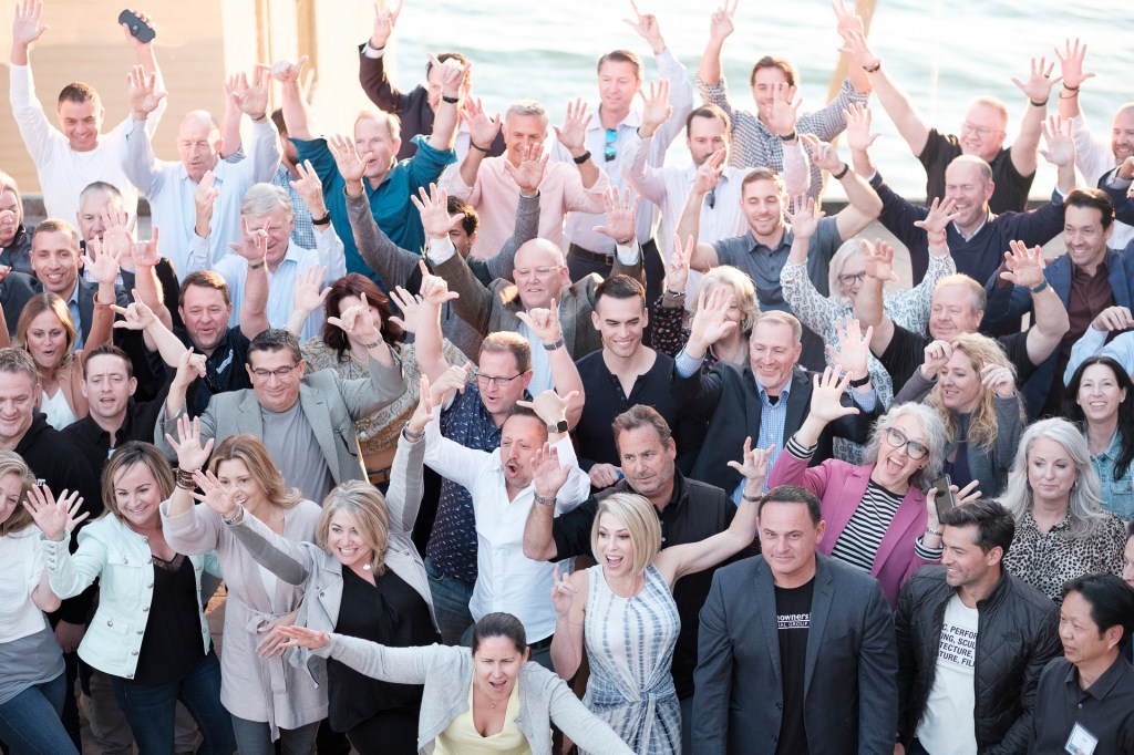 Group photo of attendees at a welcome reception, with hands raised in celebration, at Surf and Sand Resort in Laguna Beach, CA. business conference surf and sand hotel laguna beach photographer nicole caldwell
