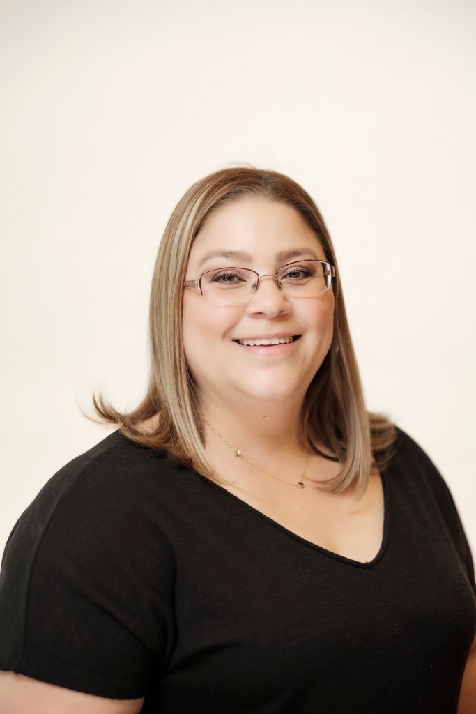 A professional headshot of a woman with glasses and light brown hair, smiling against a clean white backdrop. orange county palm springs headshot business photographer nicole caldwell