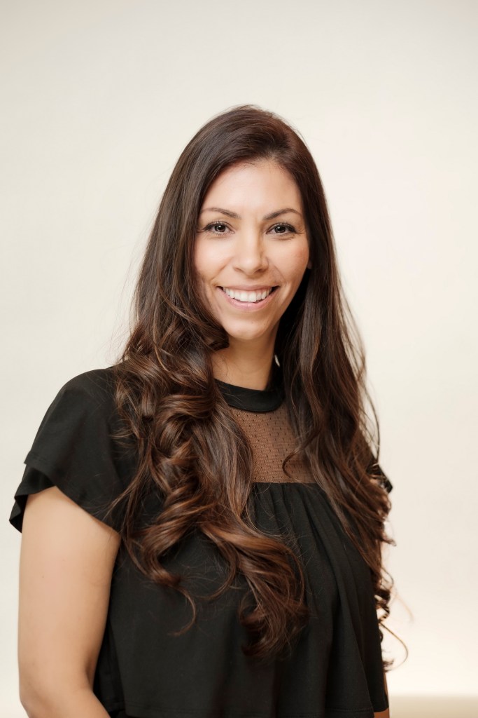 A headshot of a woman with long, wavy hair, smiling confidently against a clean white background. orange county palm springs headshot business photographer nicole caldwell