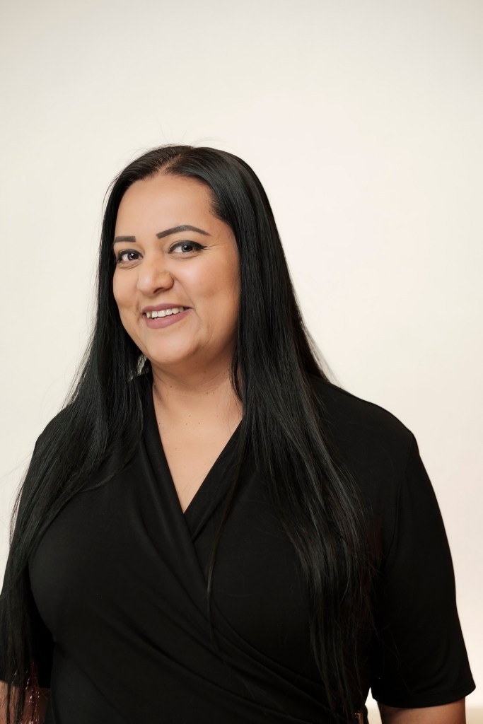 Headshot of a woman with long black hair, wearing a black shirt, smiling against a clean white backdrop. orange county palm springs headshot business photographer nicole caldwell
