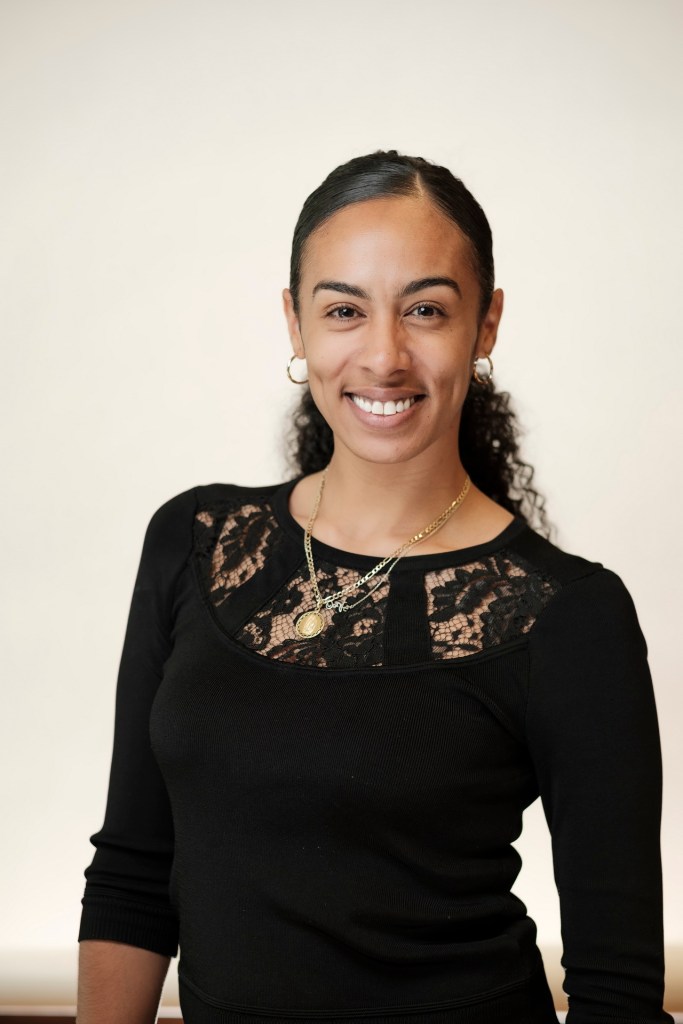 A woman smiling while wearing a black top with lace details, standing in front of a clean white backdrop. orange county palm springs headshot business photographer nicole caldwell