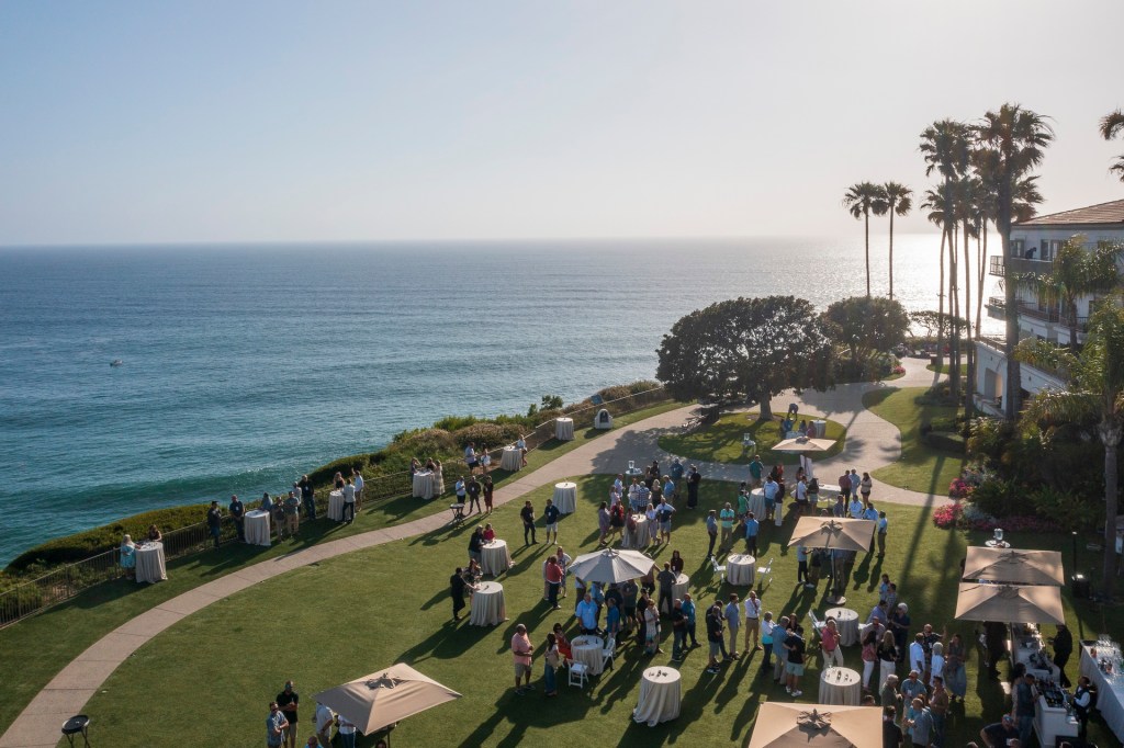 Aerial view of a gathering on a grassy area overlooking the ocean, with attendees mingling around tables and umbrellas at the Ritz Carlton in Laguna Niguel. corporate business event photographe nicole cadlwell