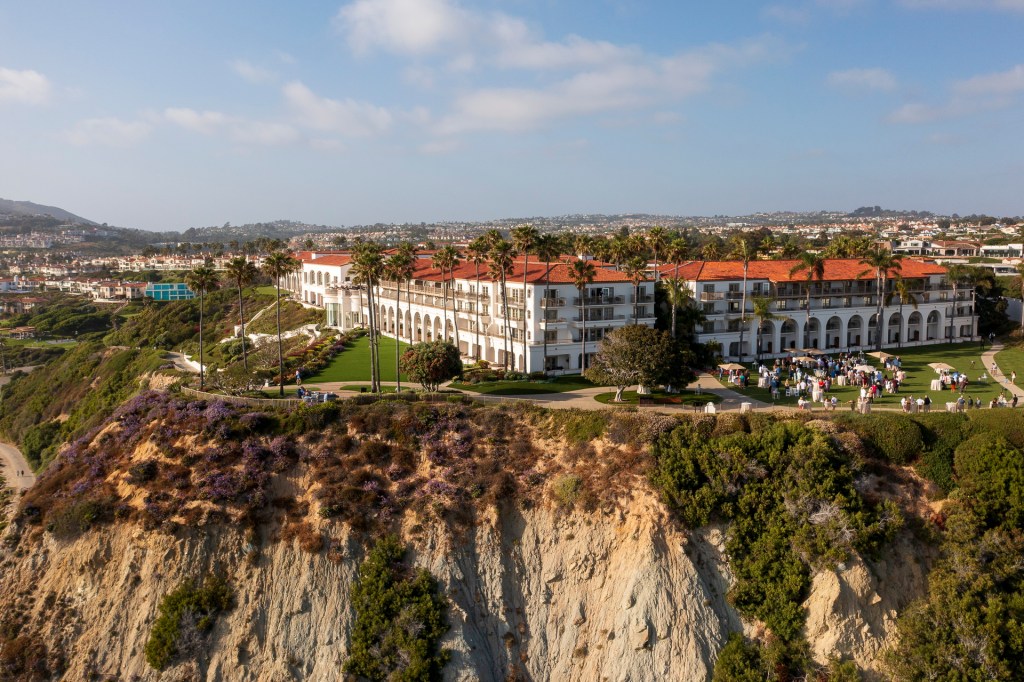 Aerial view of the Ritz Carlton in Laguna Niguel, showcasing the hotel on a cliff with palm trees and landscaped grounds, along with guests gathered for an event. corporate business event photographe nicole cadlwell