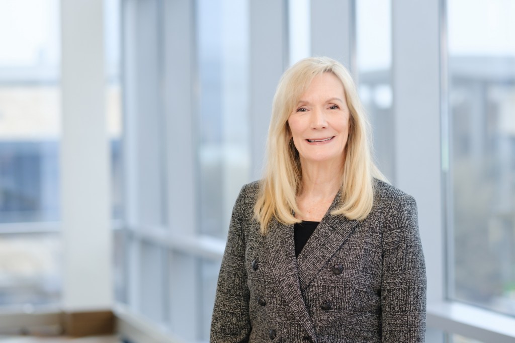 A woman with long blonde hair smiles while standing in a well-lit modern space with large windows. omni dallas headshot photographer nicole caldwell