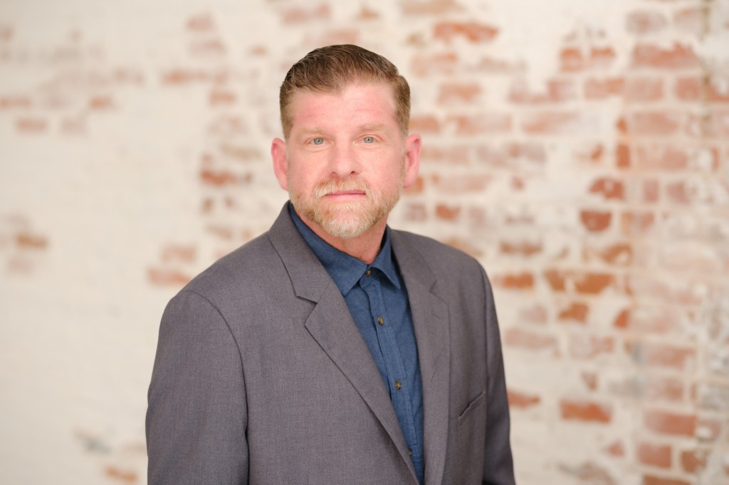 Portrait of a man in a suit standing in front of a brick wall. Orange County Photo studio for headshots nicole caldwell